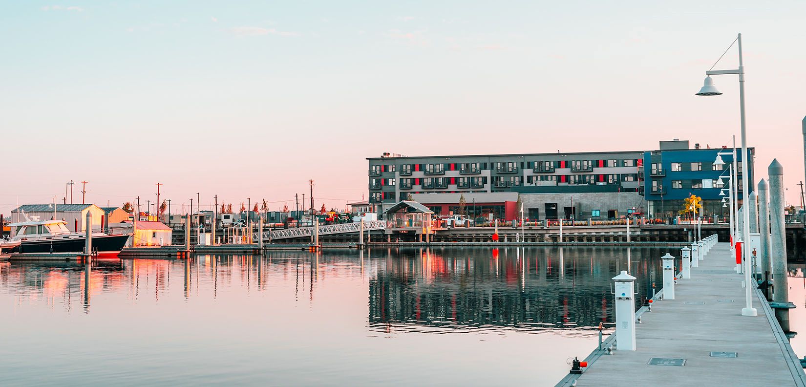 Hotel Indigo Seattle Everett Waterfront at sunset with warm lights reflecting off the marina and wooden dock