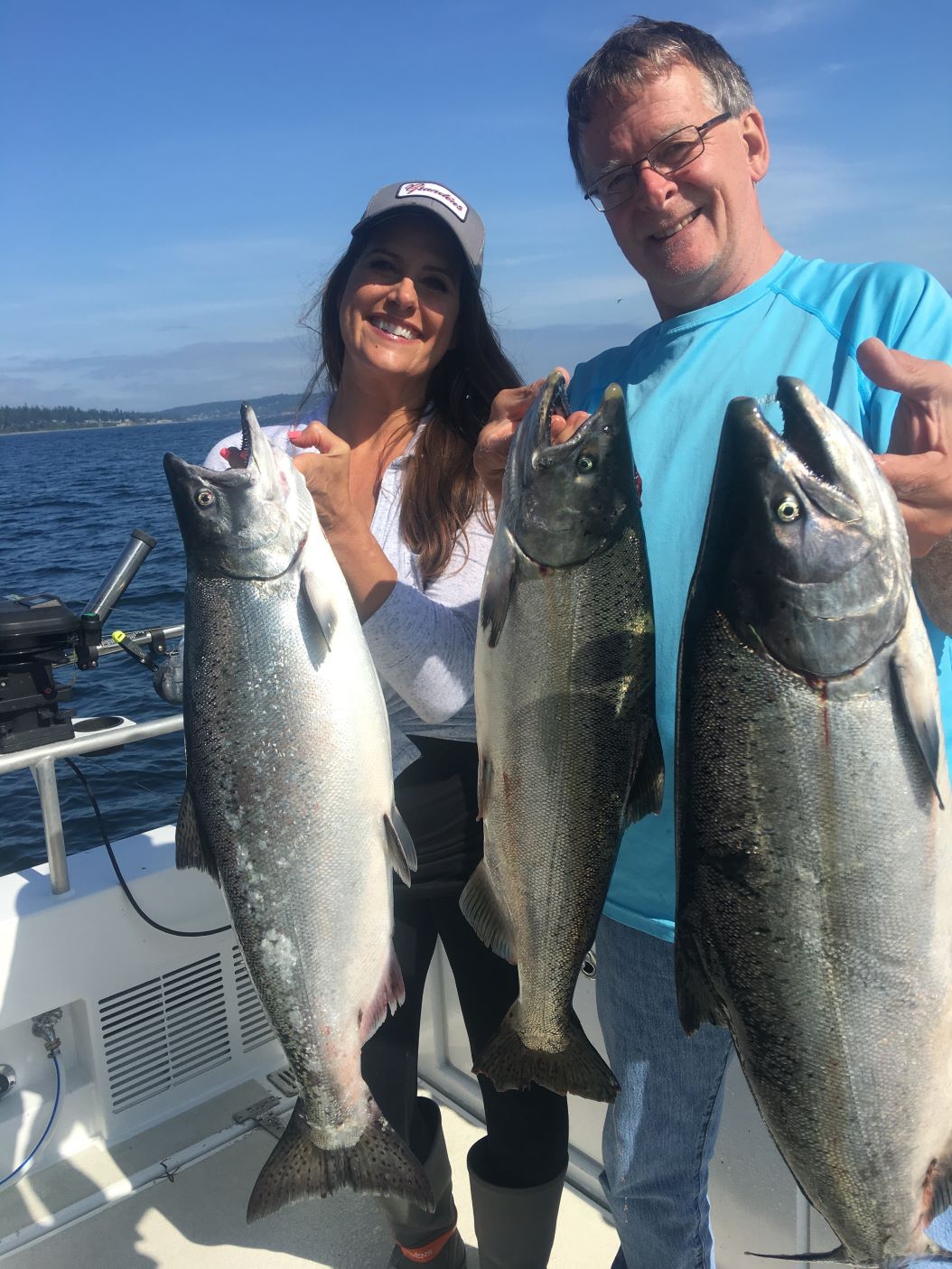 Two anglers holding multiple salmon on a bright, sunny day on Puget Sound.