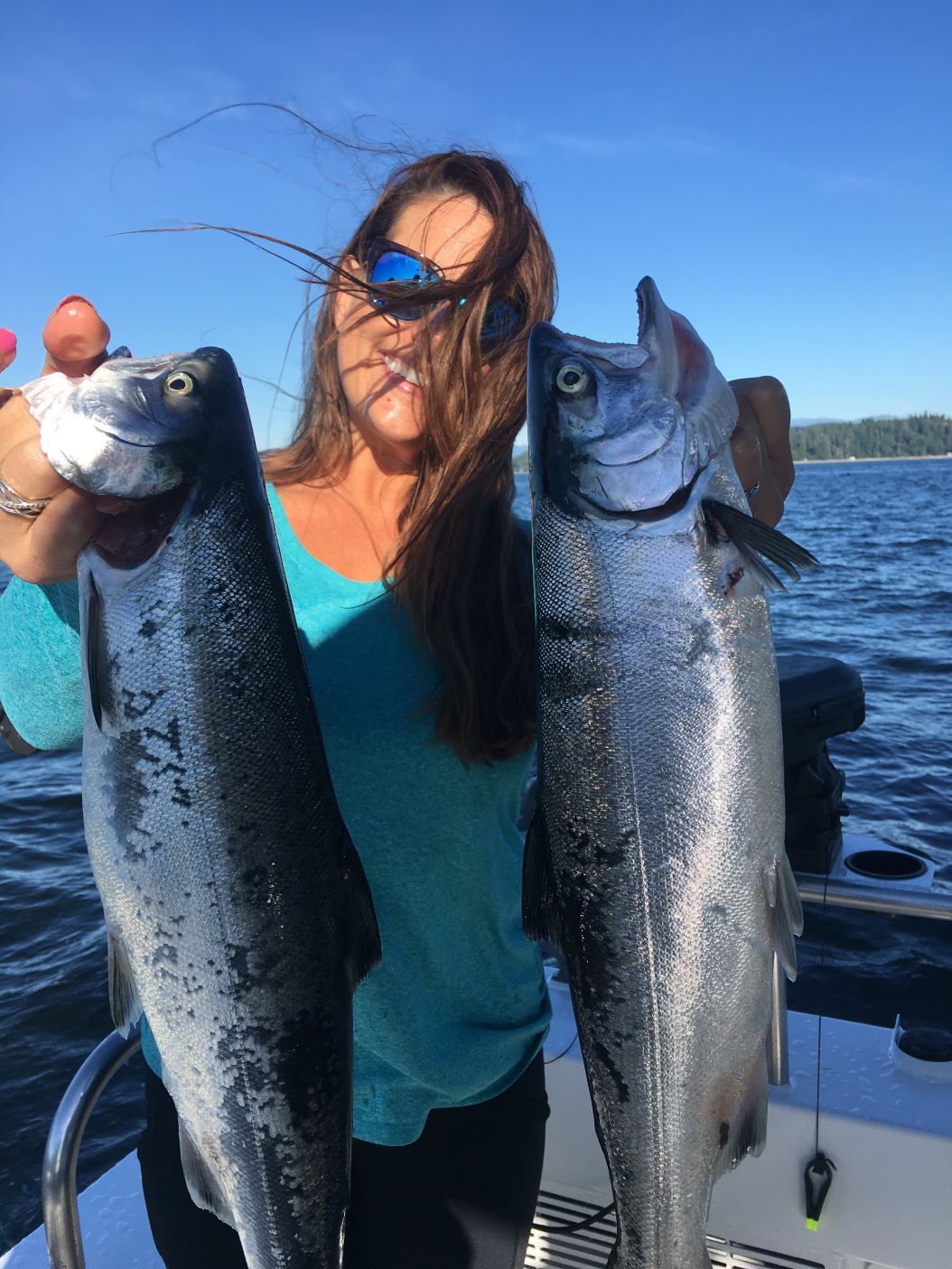 Woman holding two bright coho salmon on a sunny day on Puget Sound.