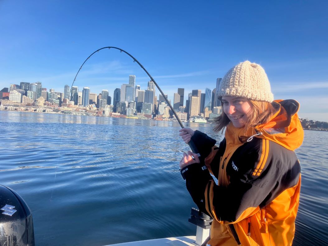 Angler smiling while fighting a fish in front of the Seattle skyline on a calm Puget Sound morning.