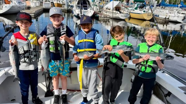 Kids proudly holding freshly caught coho salmon aboard an All Star Fishing Charters boat at Edmonds Marina near Seattle