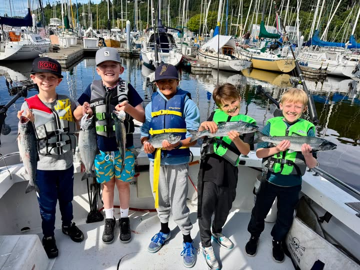 Kids proudly holding freshly caught coho salmon aboard an All Star Fishing Charters boat at Edmonds Marina near Seattle